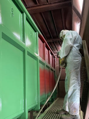 Ein Maler streicht einen Abrollcontainer in grüner Farbe